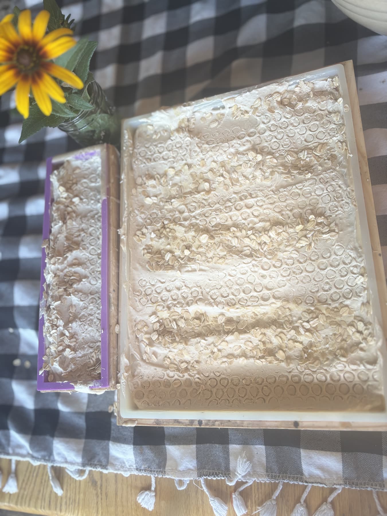 A fresh slab of soap setting in its mold, with a sunflower beside it